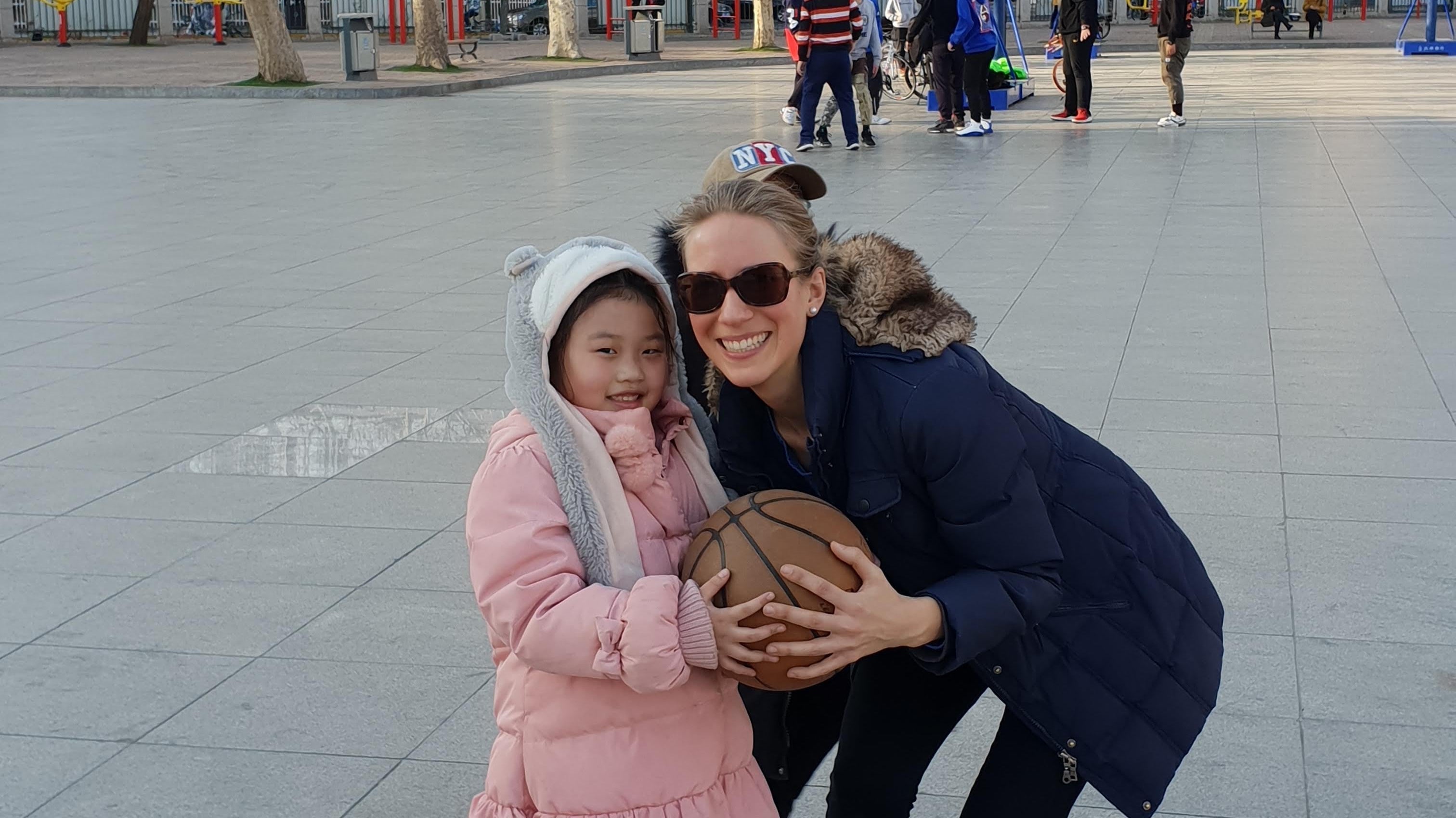 Franziska crouching with a young child holding a ball on a city square during her trip to Asia.