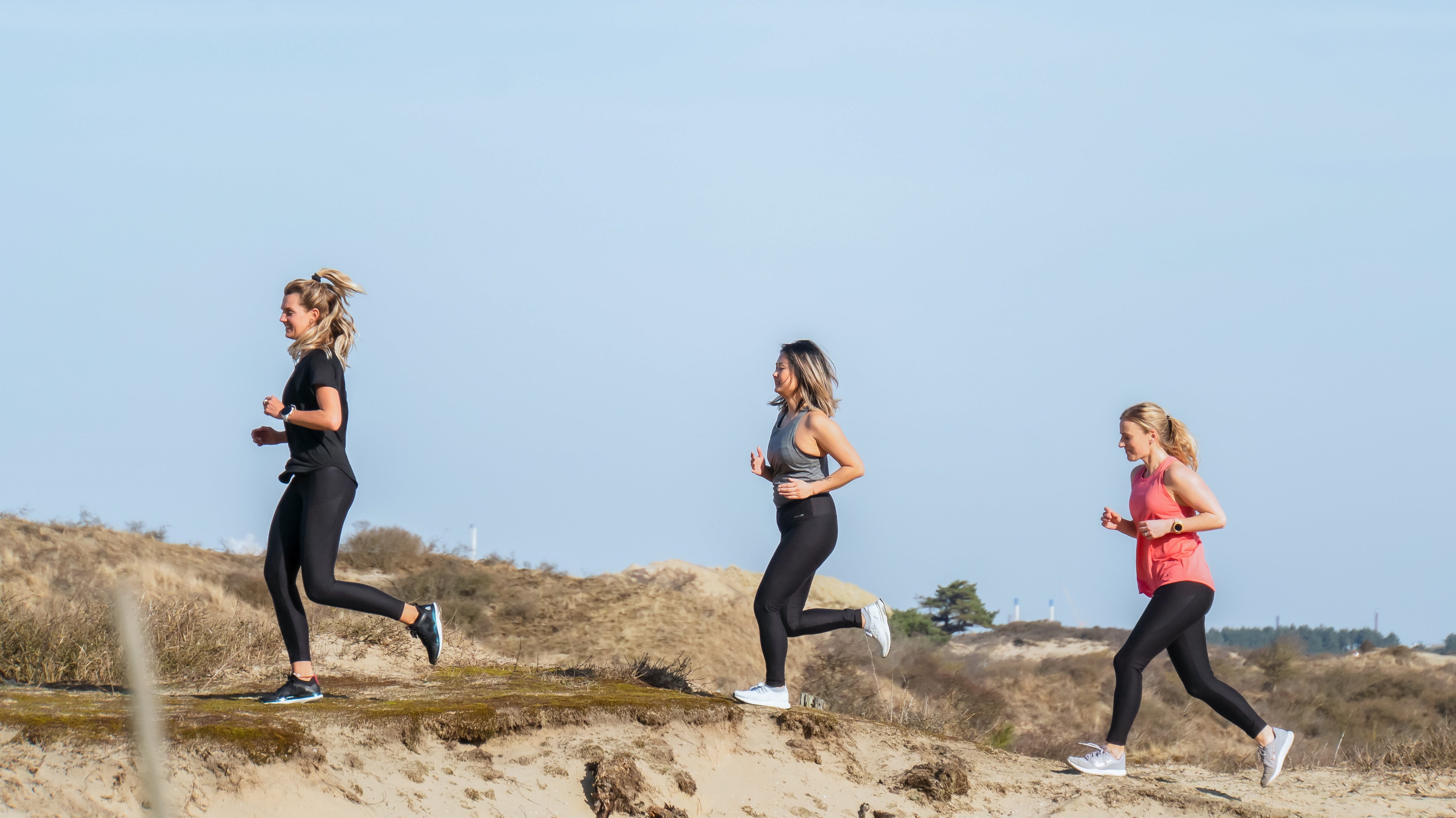 Three runners in Tripulse activewear running over coastal dunes.