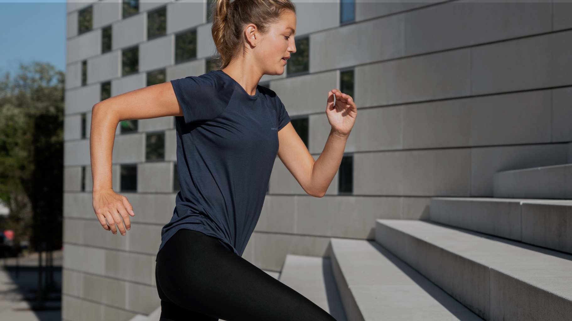 Woman running up concrete steps in a navy Tripulse T-shirt and leggings.