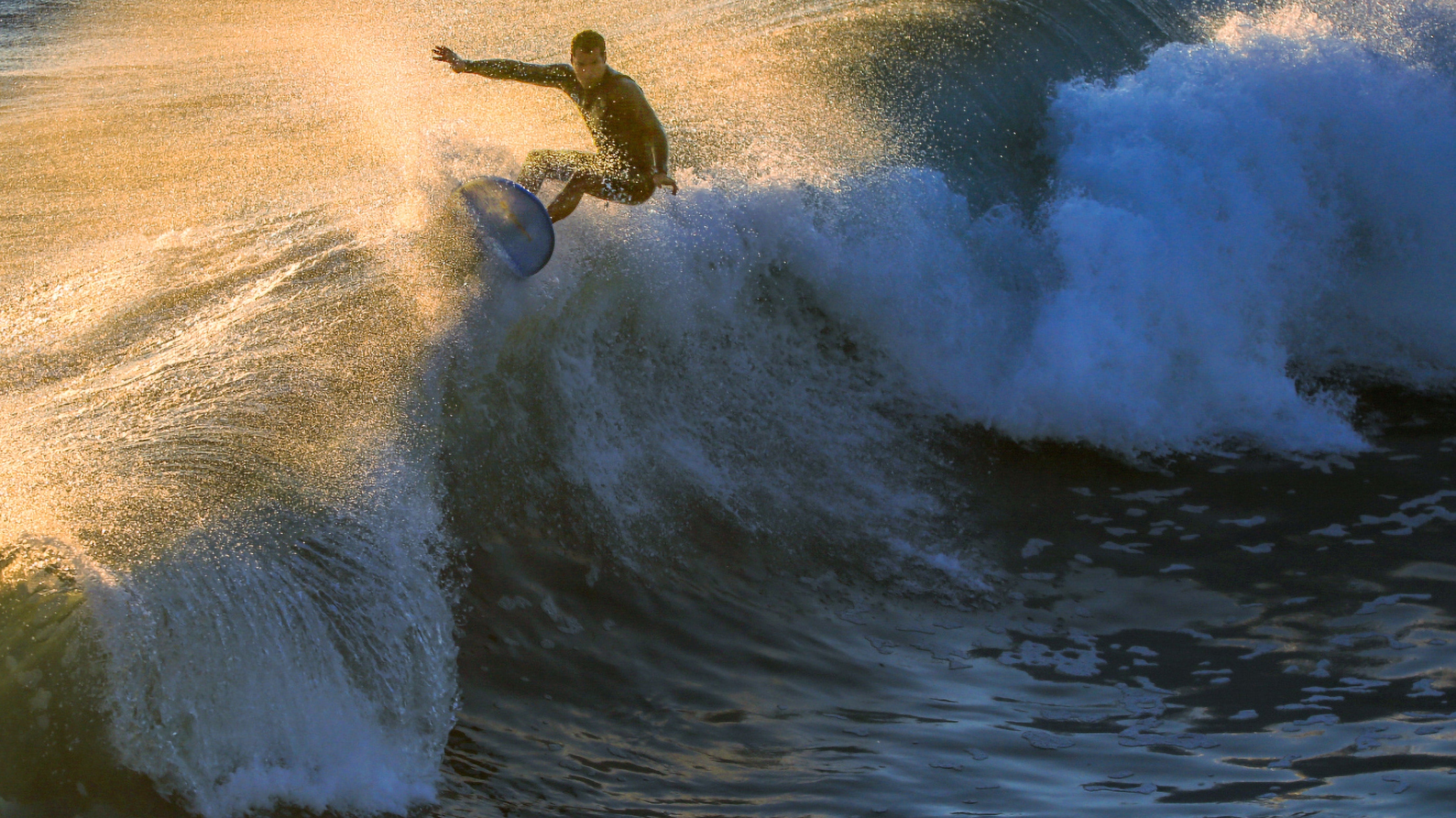 Surfer riding a breaking wave at golden hour.