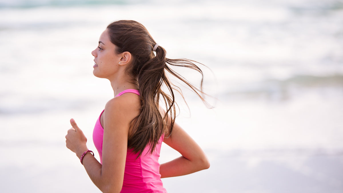 Woman running along the shoreline in a pink tank top.