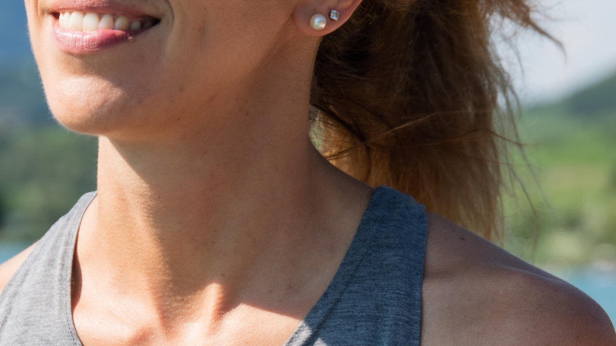 Smiling woman in sunglasses and a grey Tripulse tank top by a lake.