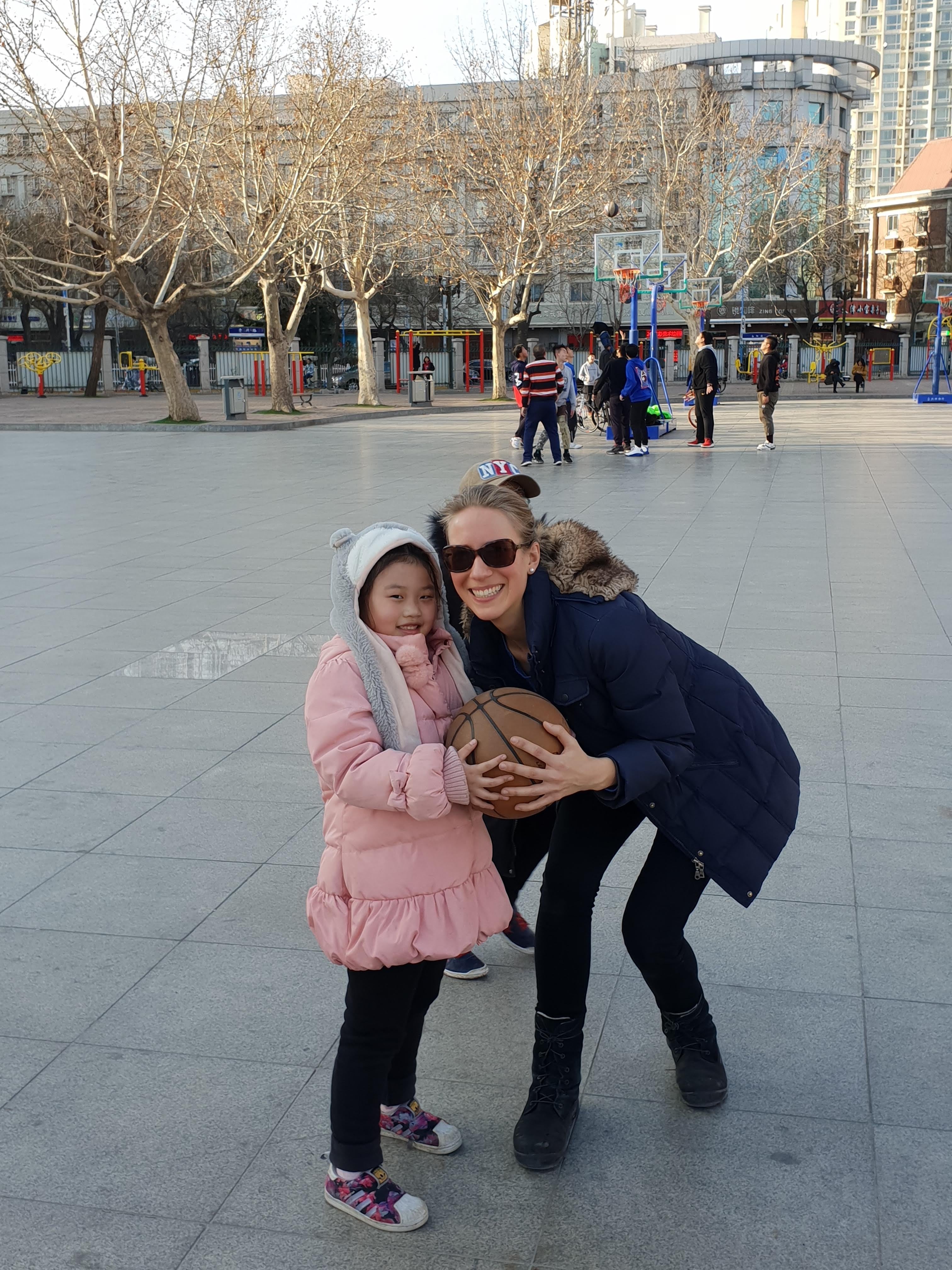 Franziska crouching with a young child holding a ball on a city square during her trip to Asia.