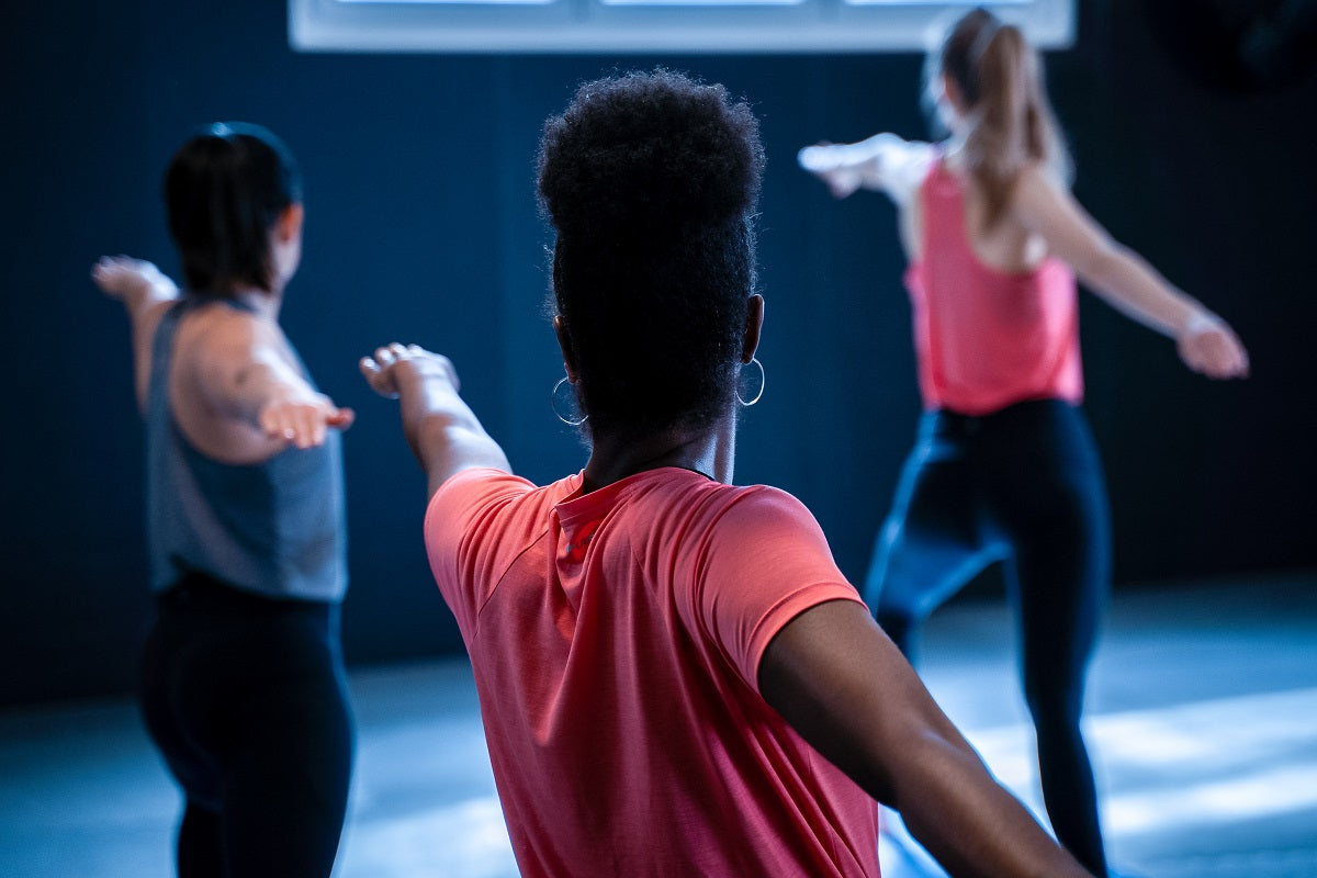 Dancers stretching in a studio wearing coral and white tops.