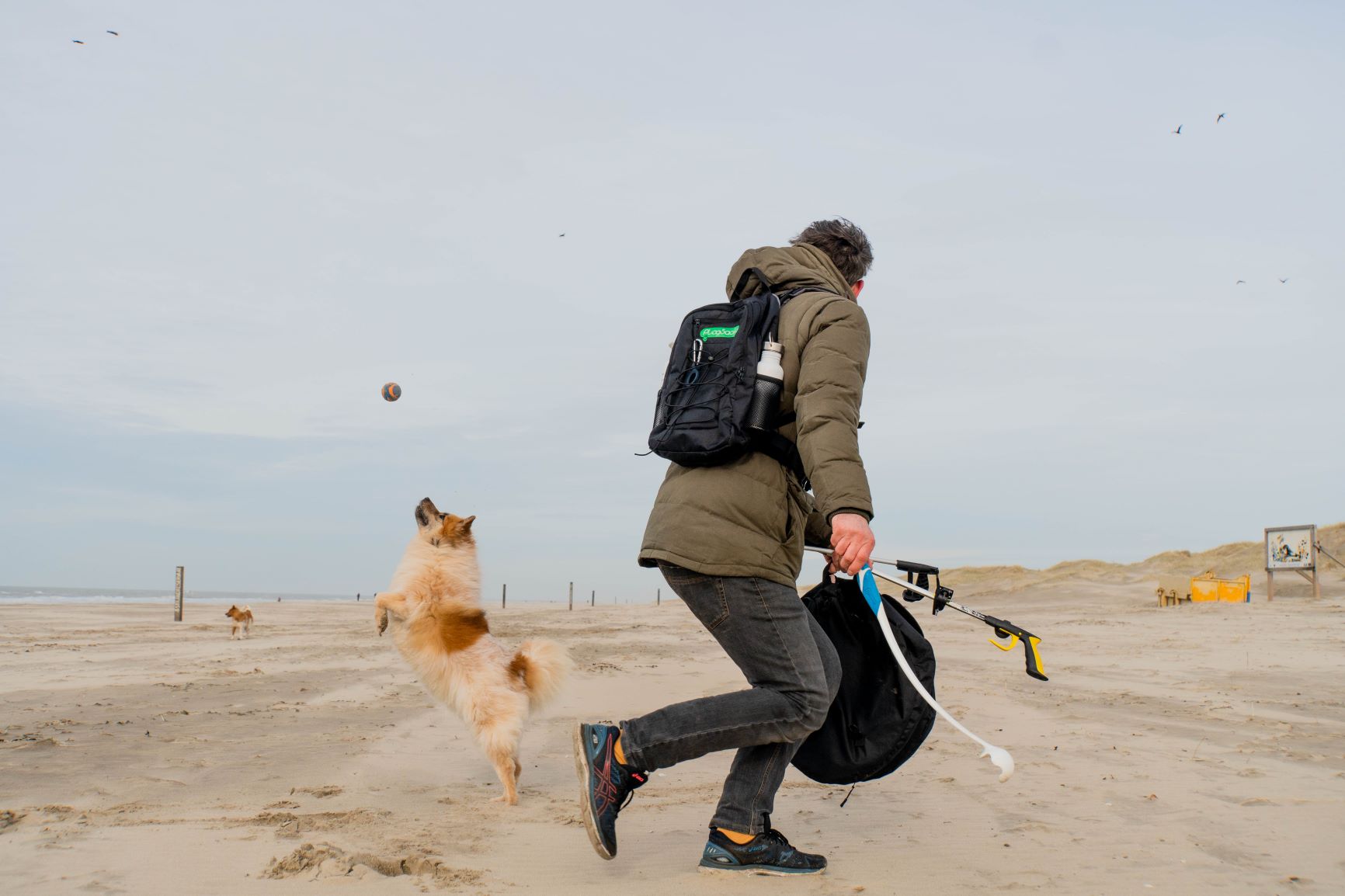 Plogger Daan Strang playing with his dog on a beach while collecting litter.