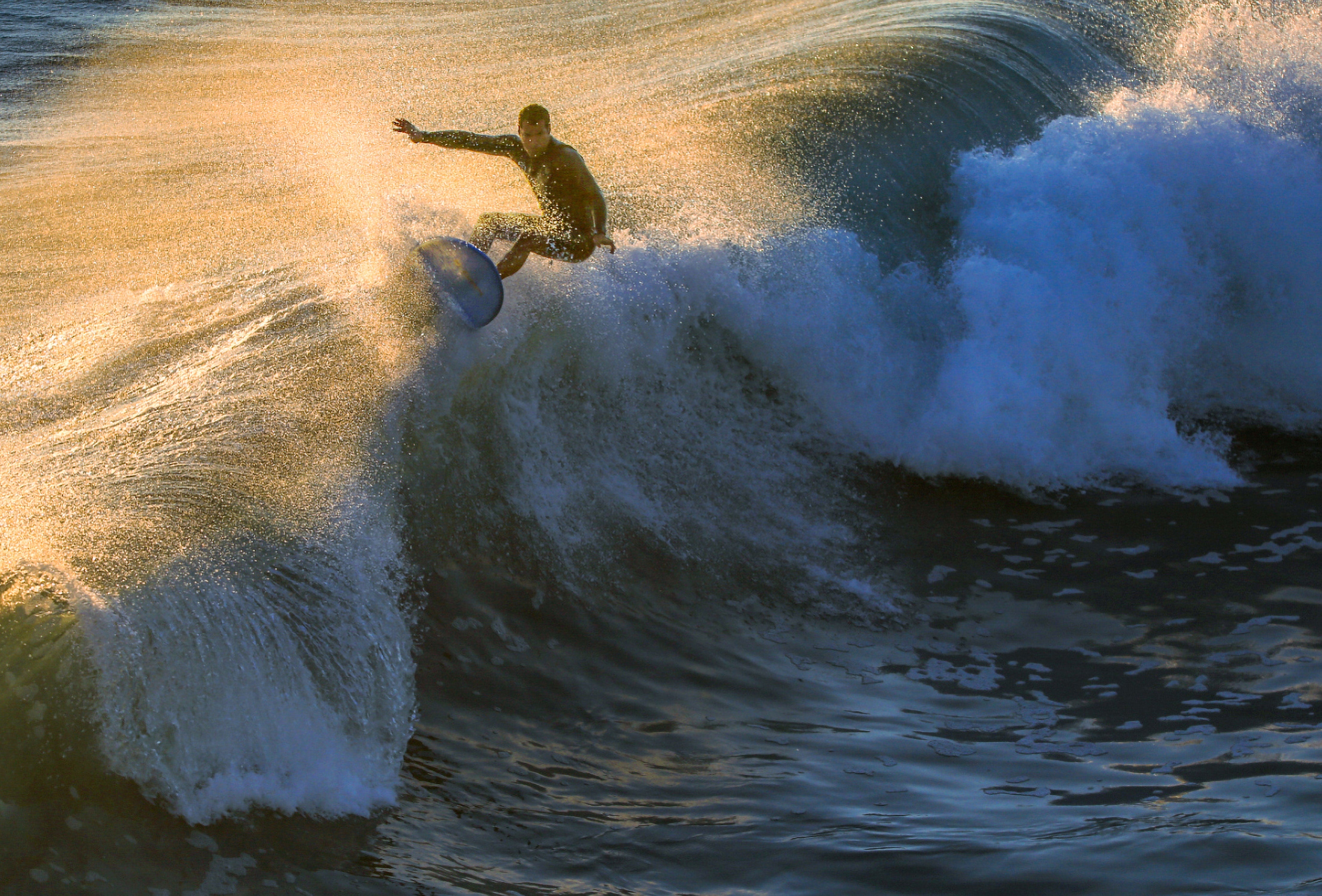 Surfer riding a breaking wave at golden hour.