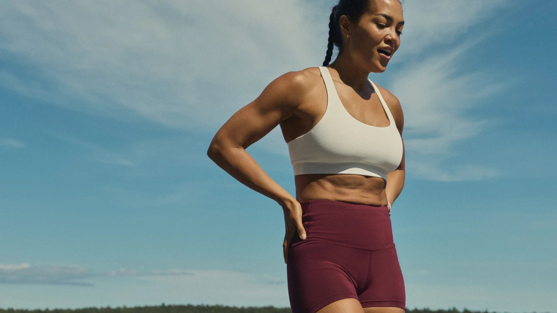 Woman cooling down after a workout in a white TENCEL™ Lyocell sports bra and wine-red Tripulse shorts.