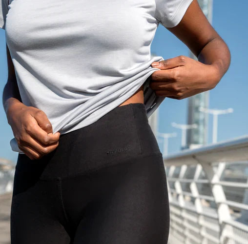 Woman lifting her white T-shirt to show the waistband of black TENCEL leggings.