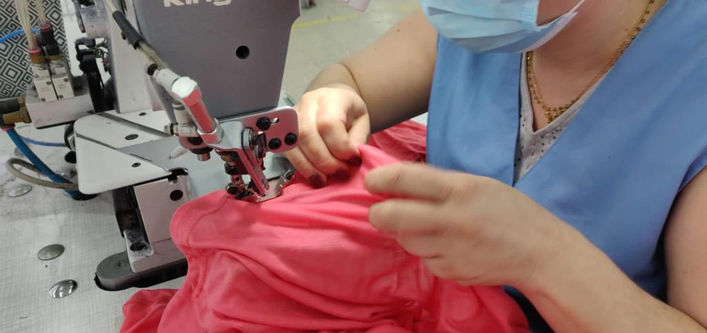 Seamstress sewing a coral garment at a factory sewing machine.